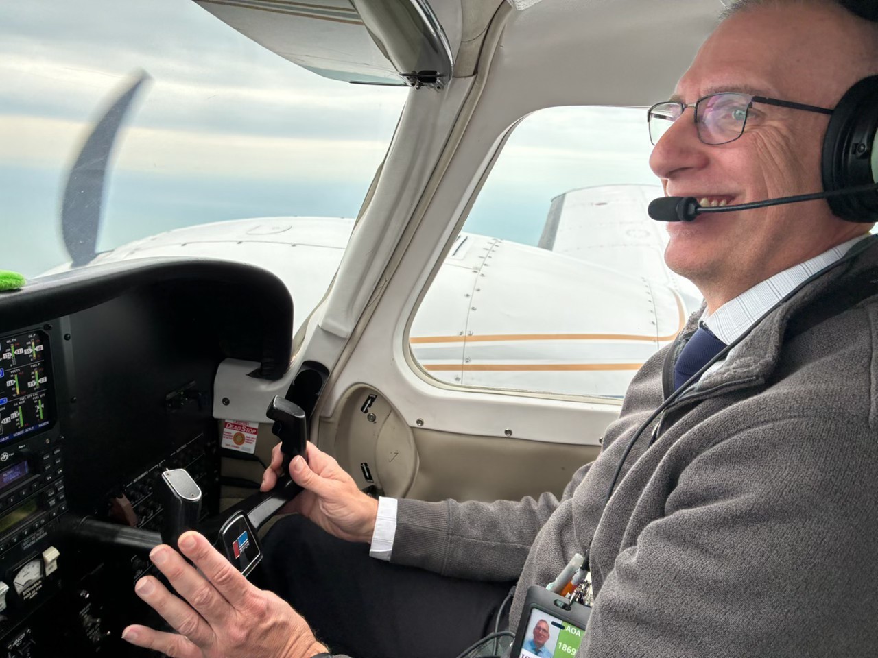 Tim flying a small aircraft, smiling in his headset with his hand on the throttle and the wing visible through the window